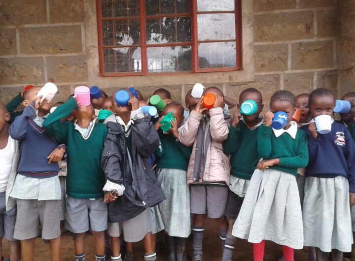 Group of African school children in uniform drinking from colorful cups as part of a corporate social responsibility nutrition program.